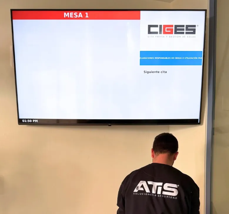 Técnico de ATISoluciones ante una pantalla de turnos CIGES instalada en la pared